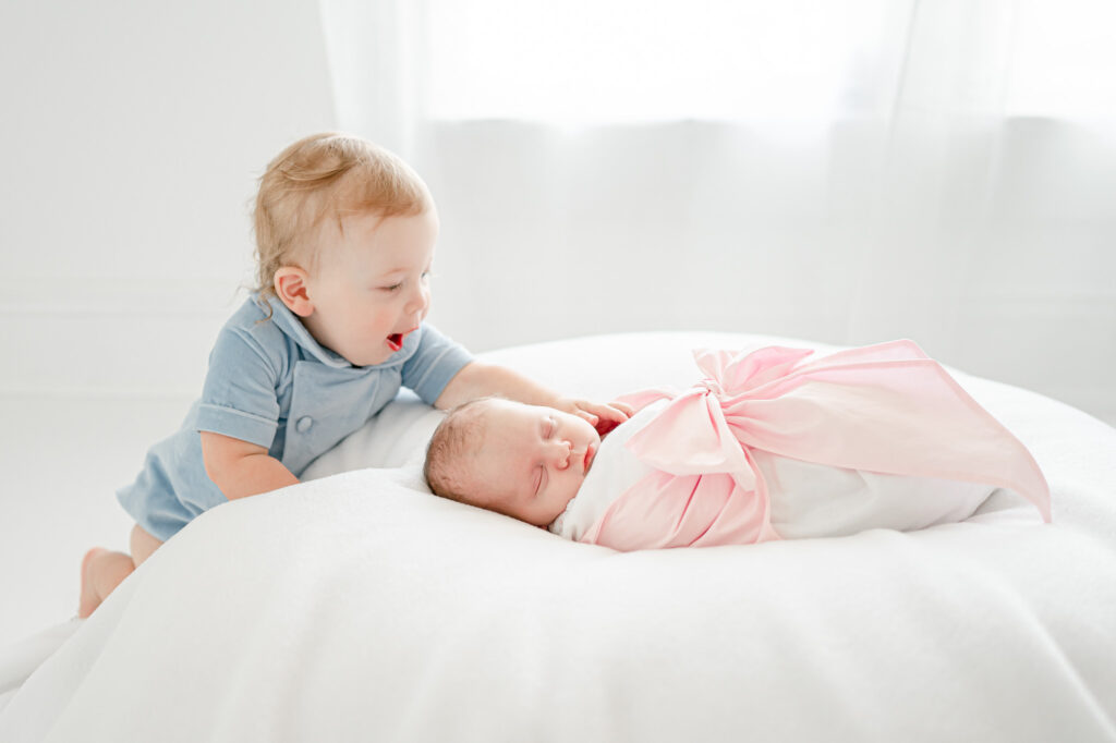 Toddler boy pats his baby sister laying on a posing bean bag.