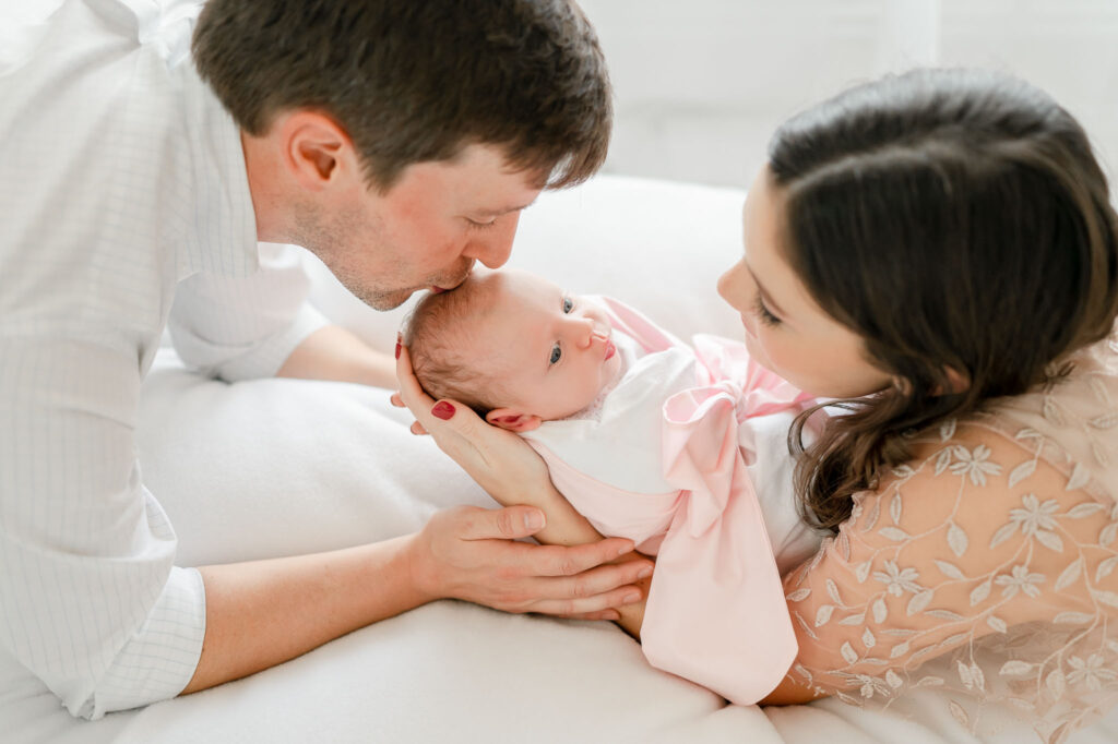 Father kisses his newborn baby's head over a posing bean bag