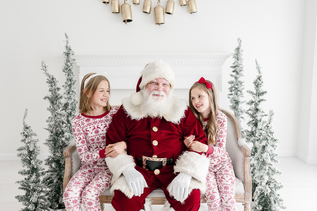 Two sisters in Christmas pajamas smile at Santa Claus