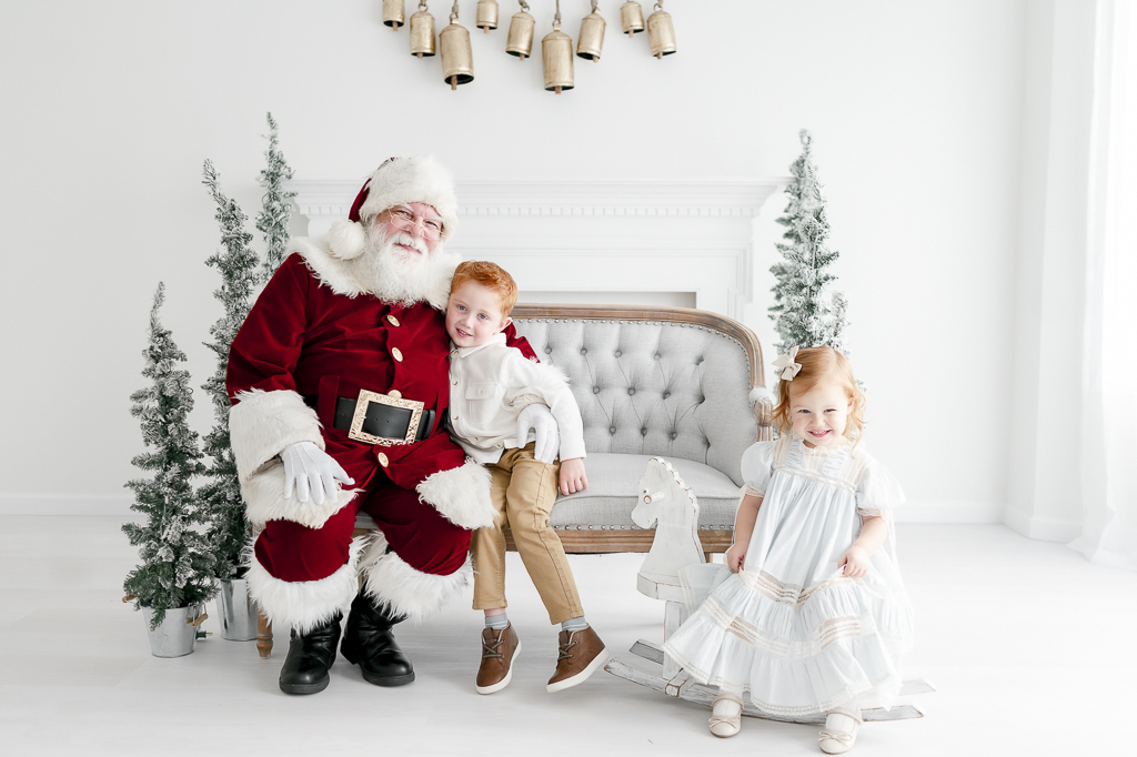 Santa hugs a red haired little boy while his sisters sits on a rocking horse in Kristie Lloyd's studio in Franklin, TN