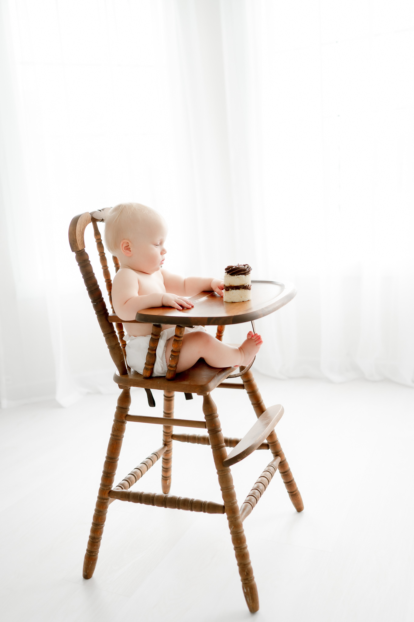 Baby sits in high chair with a chocolate smash cake