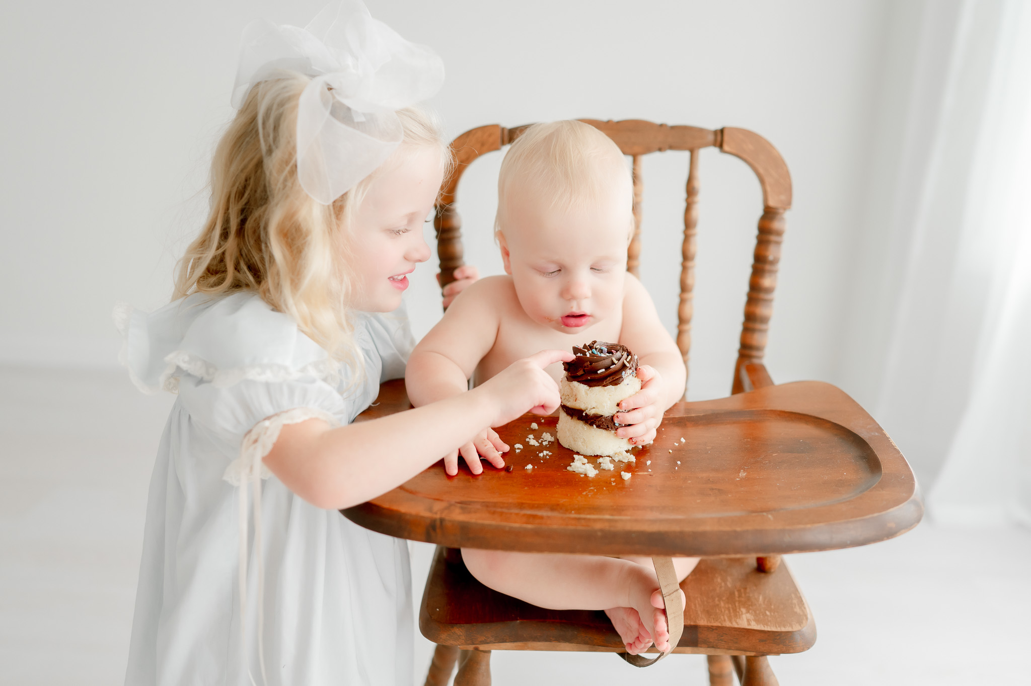 A toddler sister tastes her baby brothers smash cake