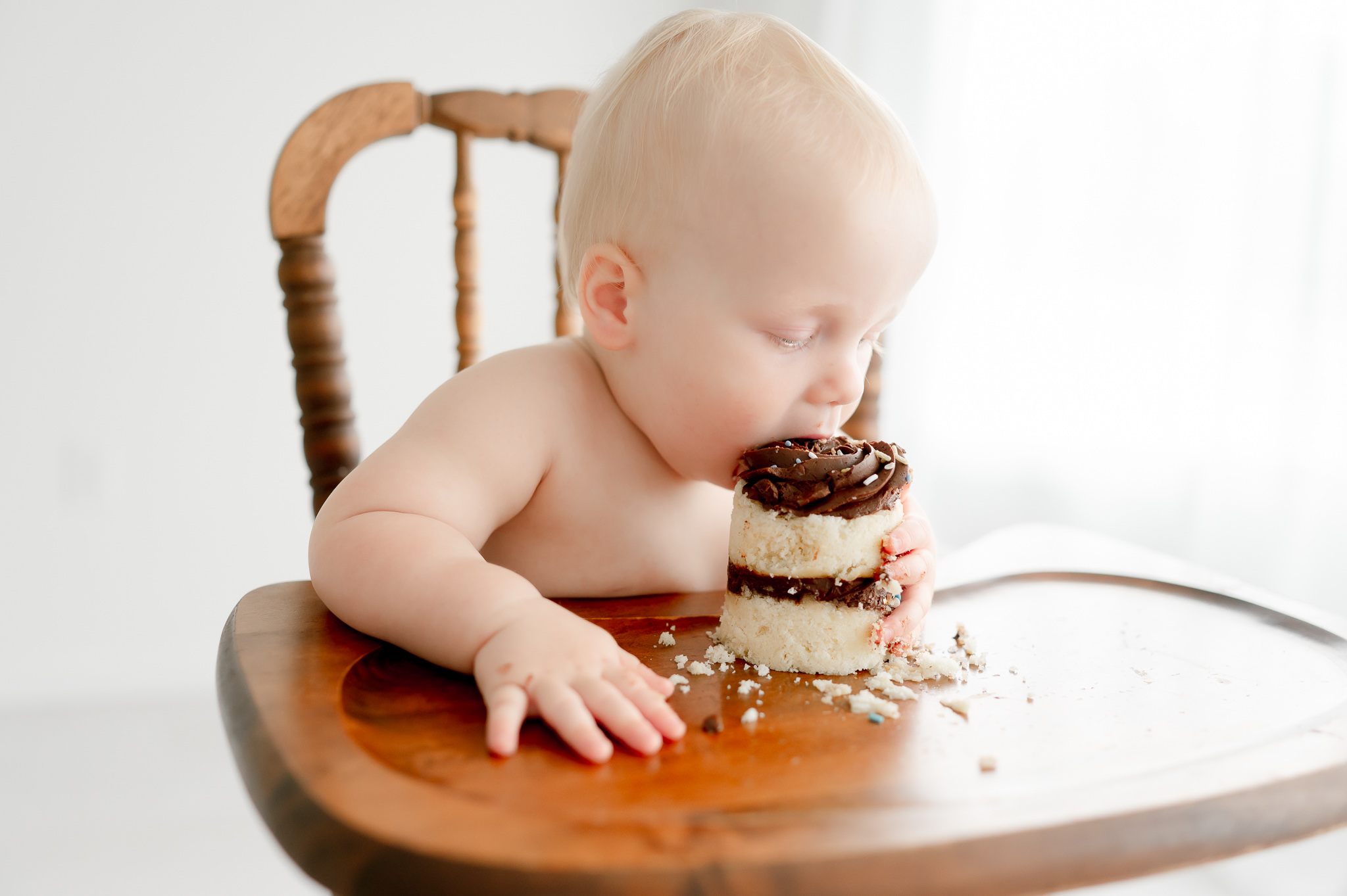 A baby bites into his smash cake sitting in a high chair