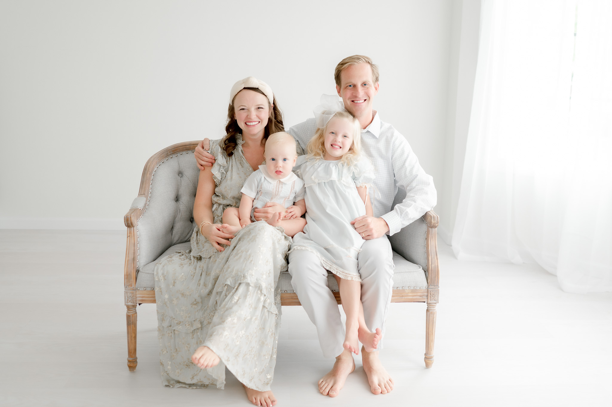 Family of 4 sits on a bench in Kristie Lloyd's photography studio