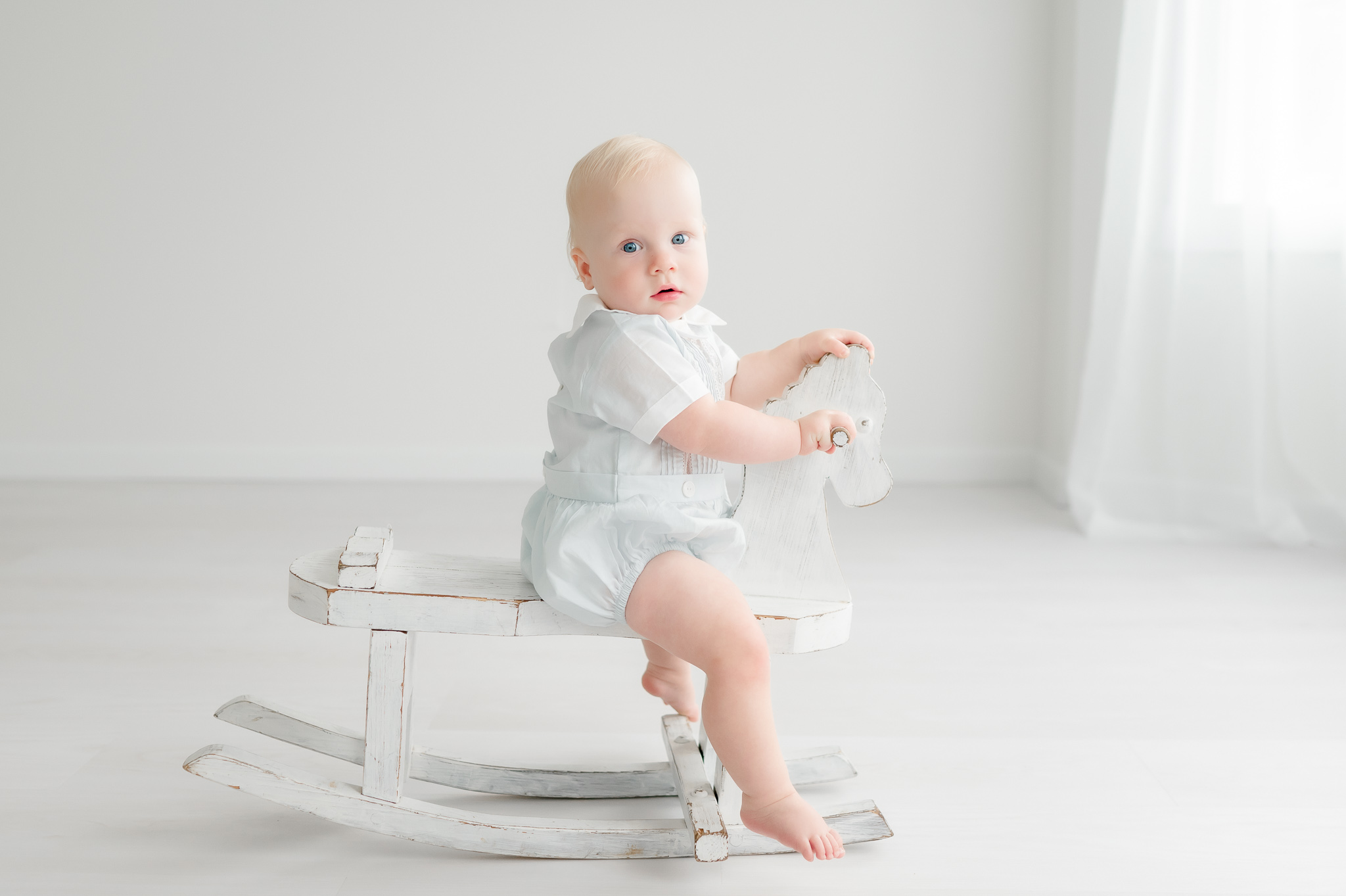 Baby boy sits on a white rocking horse