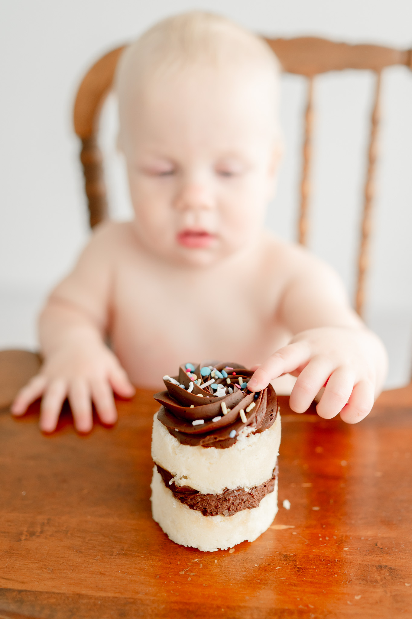 Baby puts his finger in a chocolate cupcake with sprinkles