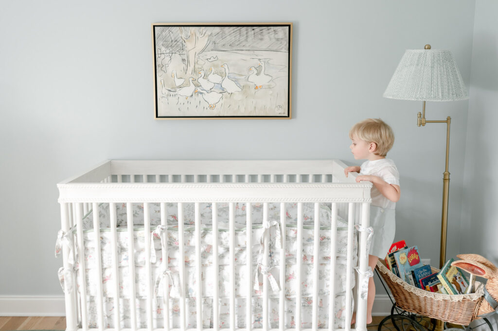 Little boy peeks into his brother's crib in a grandmillenial nursery 