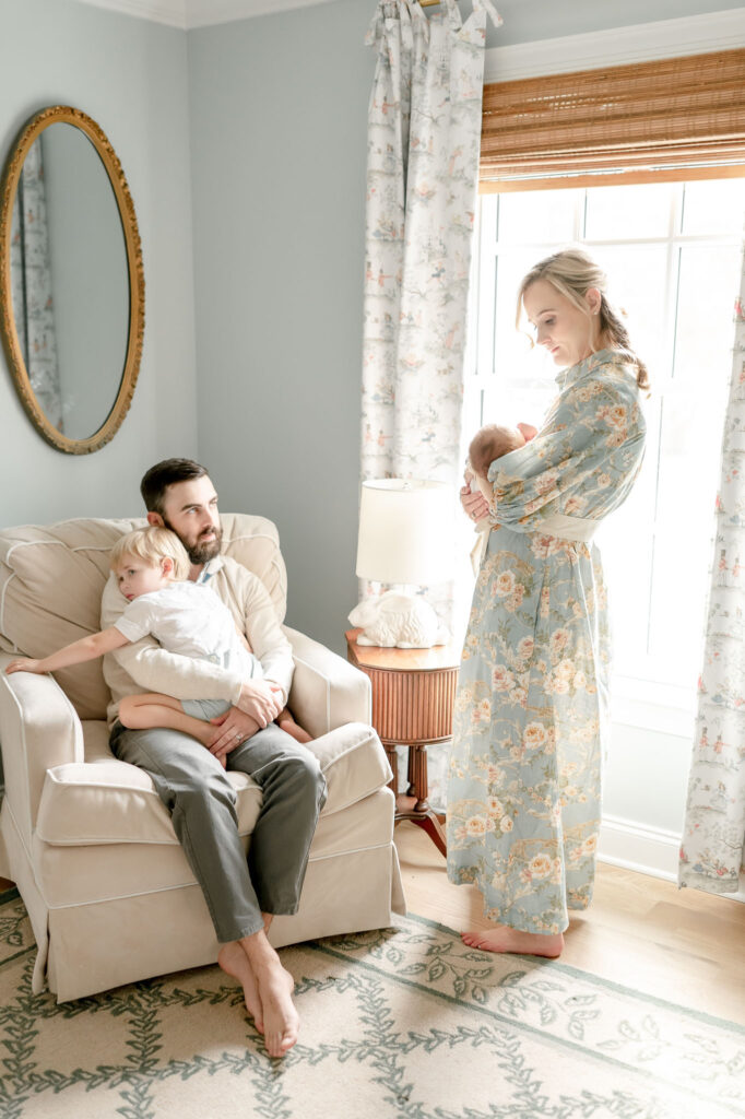 A mother stand by a grandmillenial nursery window holding her newborn 