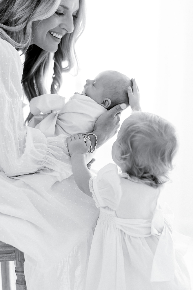 Black and white image of a mother smiling at her newborn and toddler
