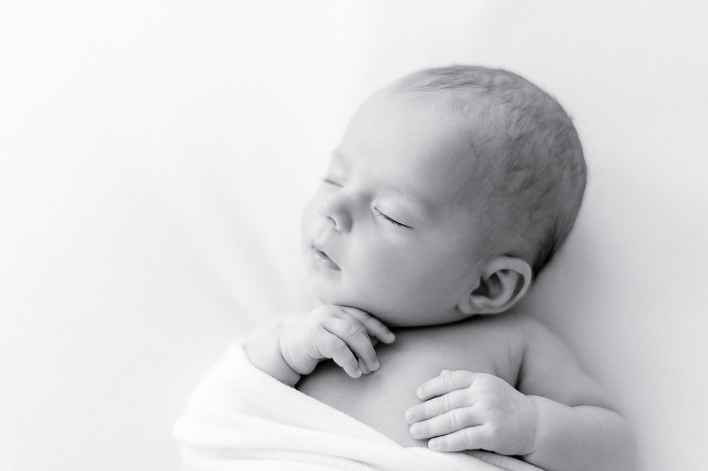 Black and white image of a newborn in a white swaddle