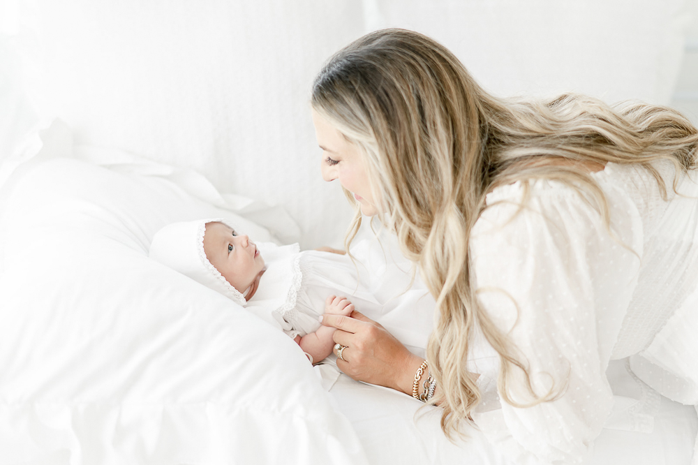 A mother smiles at her baby wearing a white bonnet in Kristie Lloyd's studio
