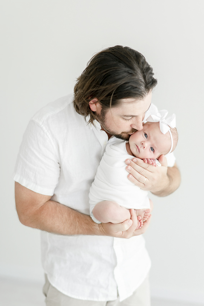 A father kisses his baby as she looks at the camera