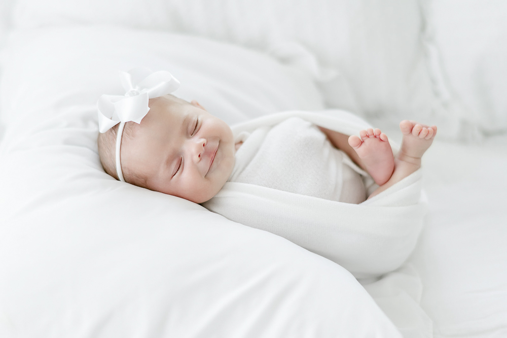 A newborn smiles in her sleep laying on a white pillow