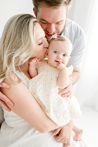 A mother kisses her baby as her husband hugs them both