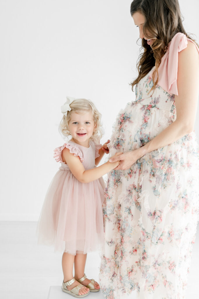 A pregnant mother smiles down at her daughter as she holds her hands