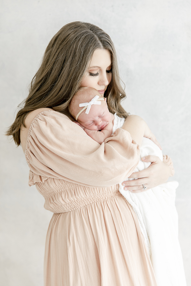 A mother in a pink dress holds her newborn baby to her chest