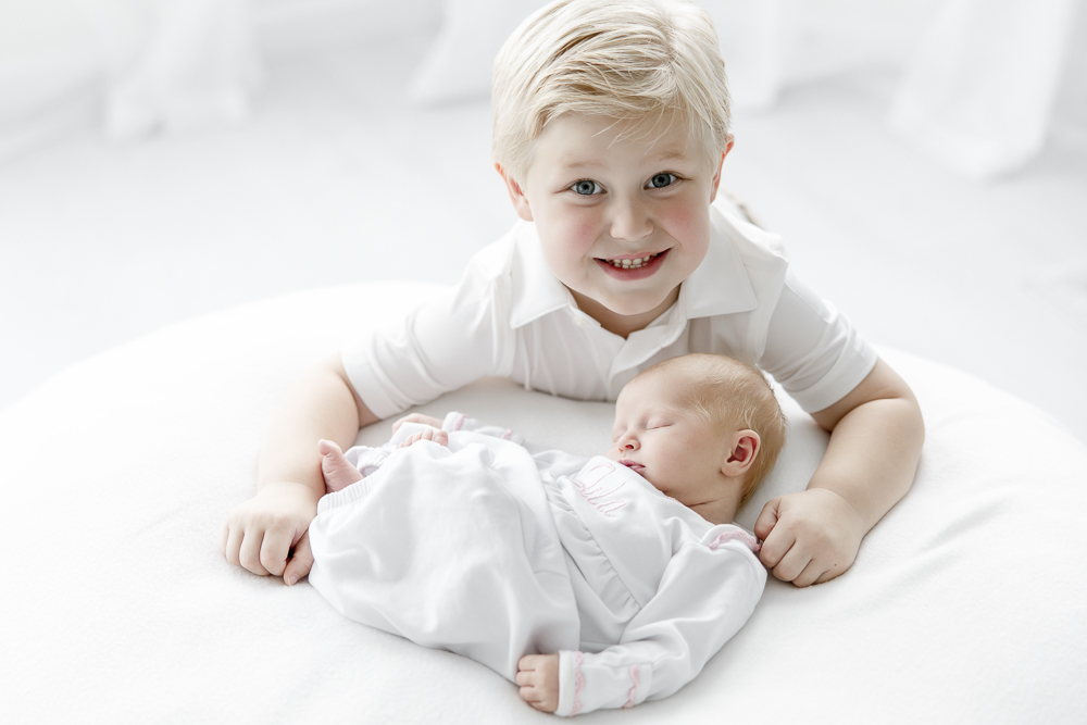 A blonde boy smiles as he holds his newborn baby sister